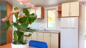 Cocina compacta con lavaplatos, estufa y refrigerador, una mesa de comedor con una silla, y una planta en maceta.