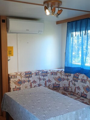 Ein Zimmer mit einem Bett, einem Fenster mit blauen Vorhängen, einer Klimaanlage und einem gemusterten Sofa.