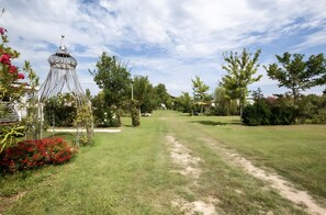 Um gramado bem cuidado, uma estrutura metálica decorativa e diversas árvores.