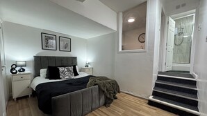 Une chambre à coucher comprenant un lit, des tables de chevet, une fenêtre et un escalier menant à une salle de bain.
