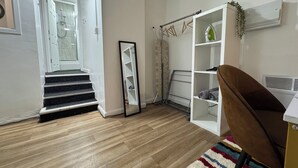 Un appartement moderne avec un plancher en bois, un escalier menant à une salle de bain, une armoire blanche et un fauteuil marron.