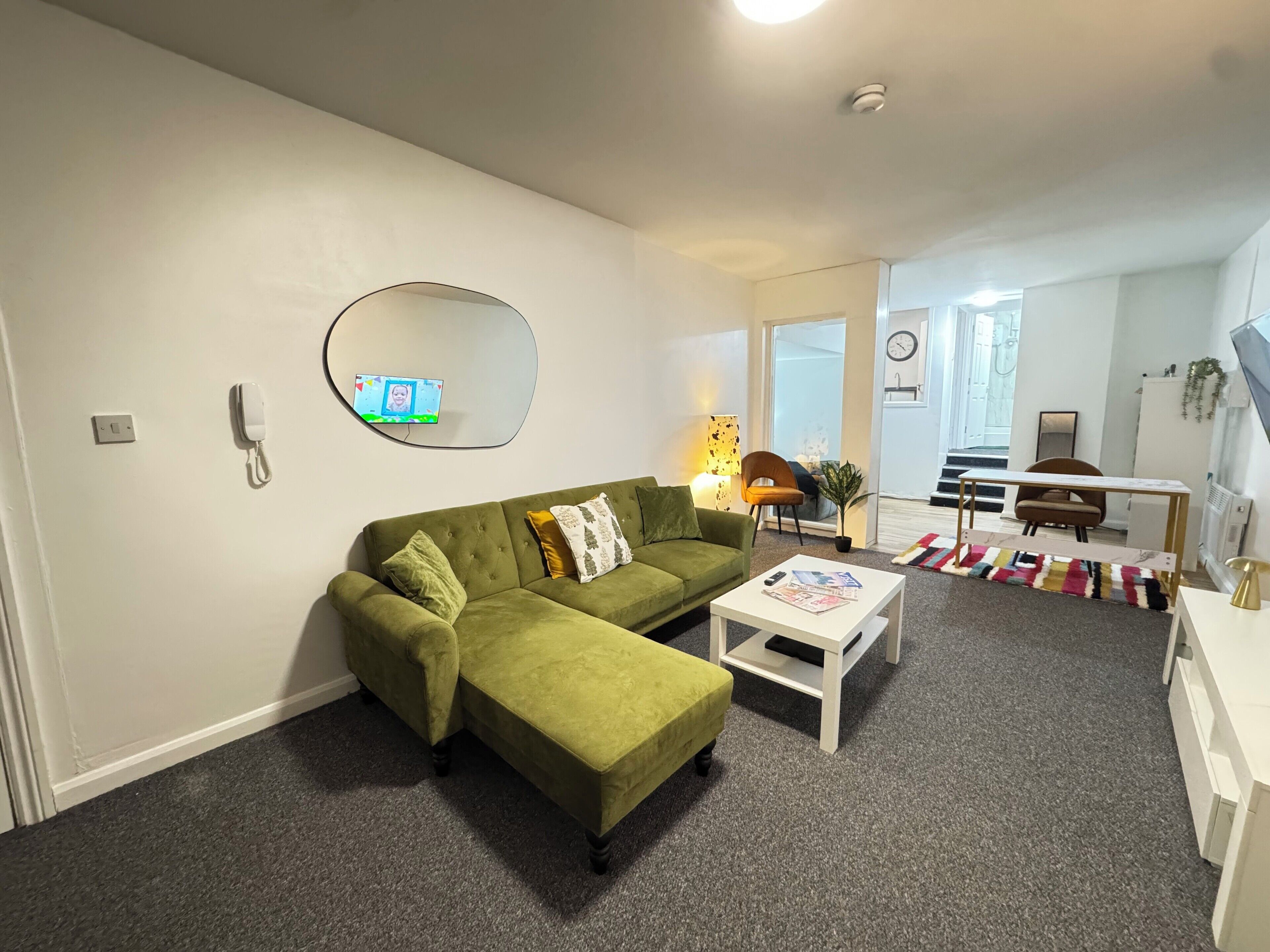 A living room with a green sofa, a white coffee table, and a mirror on the wall.