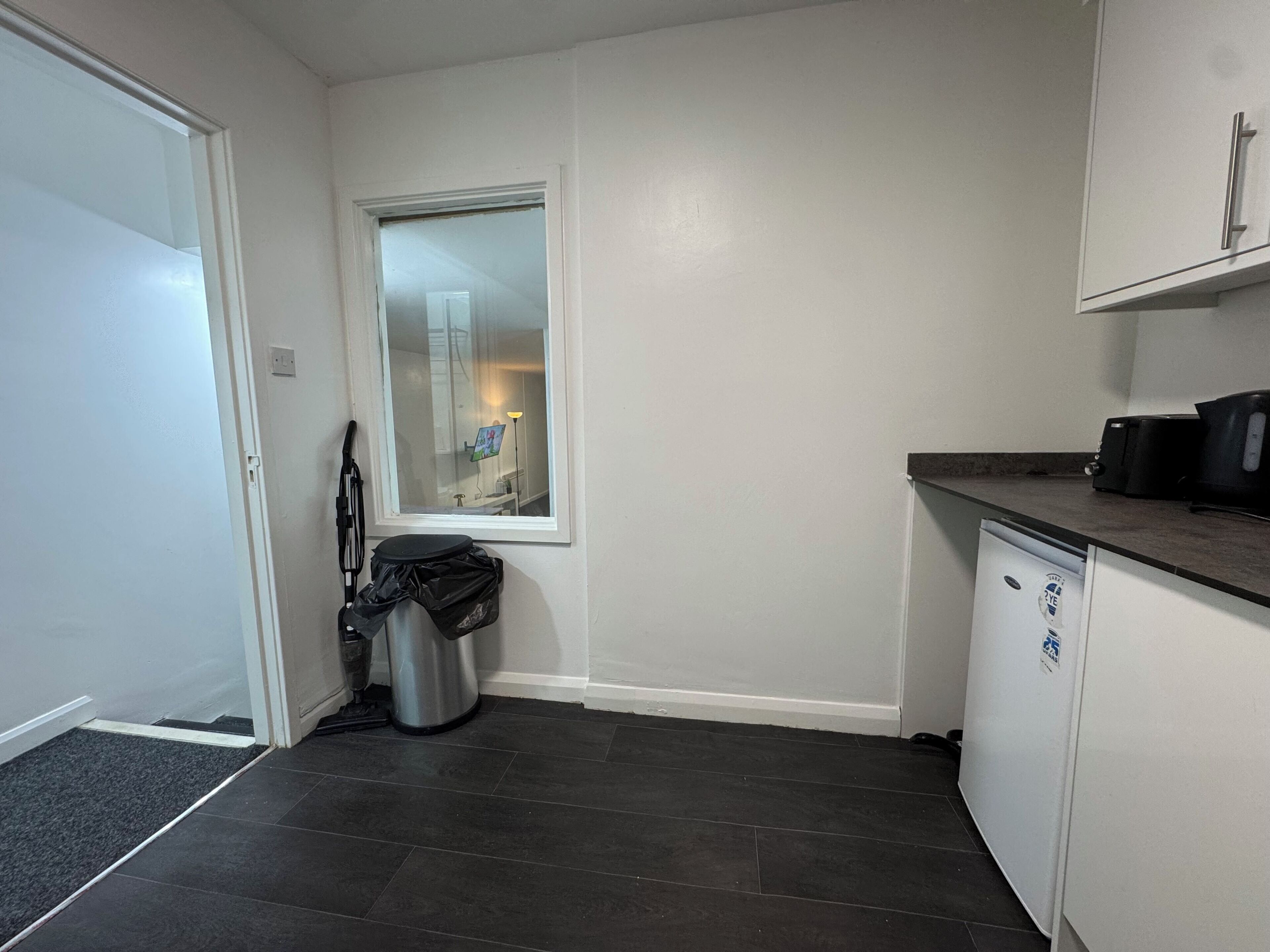 Eine kleine Küche mit Fenster, Mülleimer, Geschirrspüler und einer Arbeitsplatte mit Toaster.
