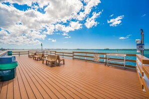 A wooden deck with benches and a trash bin, overlooking a body of water with a clear sky. - Walk Downtown | Private Patio | Pool | Pets | Sunny (Dunedin)