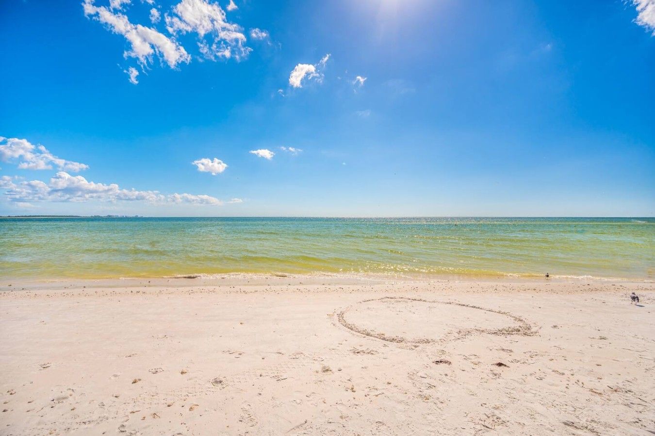 Una playa con cielo despejado, mar tranquilo y huellas en la arena.