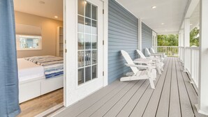 A room with a bed, a window, and a door leading to an outdoor porch with white chairs. - Boutique Tiny House Escape with Pool | Sunny (Dunedin)