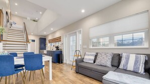 A modern living room with a grey sofa, blue chairs, and a wooden staircase leading to a kitchen. - Boutique Tiny House Escape with Pool | Sunny (Dunedin)