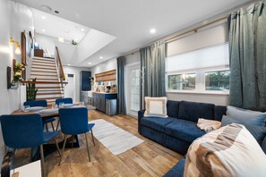 Un salon moderne comprenant un canapé, une table à manger et des chaises, un coin cuisine et un escalier menant à un niveau supérieur.