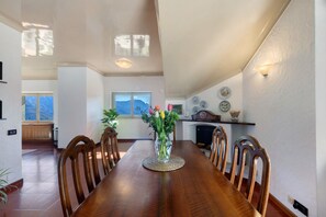 A dining room with a wooden table, chairs, a vase with flowers, and a view of the mountains through a window.
