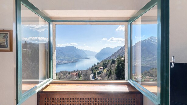 Een kamer met een groot raam met uitzicht op een meer en bergen.