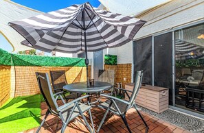 A patio with a table and chairs, a striped umbrella, and a sliding glass door. - Stylish 2BR 2BA Chandler Townhome with Vaulted Ceilings & private patio (Chandler)