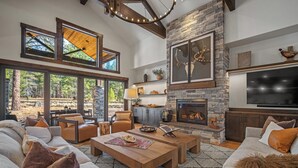 Un amplio salón con chimenea de piedra, ventanas grandes y un conjunto de asientos cómodo.