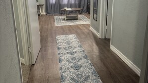 Ein Flur mit Holzboden, einem gemusterten Teppich, einem Tisch mit Pflanze und einem Spiegel an der Wand.