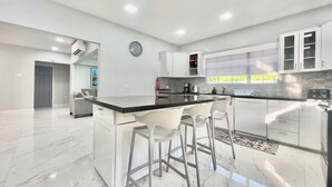 A modern kitchen with white cabinetry, a marble countertop, and a built-in island with bar stools. - NEW Luxury 4BR Family Villa | Private Pool & Spa | Gated Community (Bon Accord, Tobago, Trinidad and Tobago)