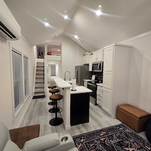A modern kitchen with a central island, a dining area with stools, and a small seating area with a rug.