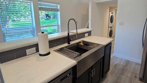 Een moderne keuken met een ingebouwde vaatwasser, een RVS spoelbak en een raam met uitzicht op een tuin.