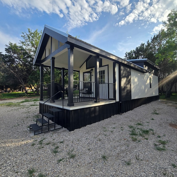 A modern house with a covered porch, a staircase, and a gravel driveway.