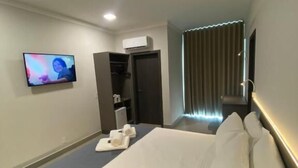 Habitació d'hotel moderna amb un llit gran, una televisió de pantalla plana penjada a la paret, un armari i una finestra amb cortines.
