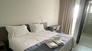 Habitació d'hotel amb un llit gran, un escriptori i una cadira. Es pot veure un bany per una porta oberta.
