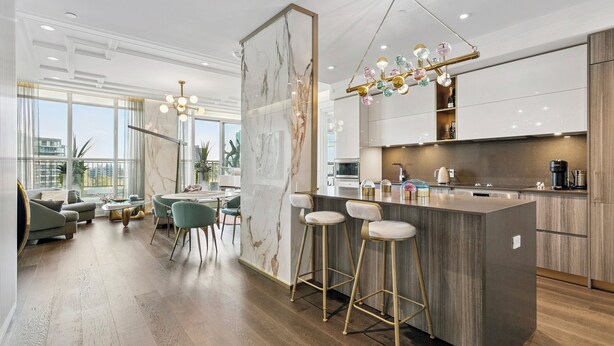 Een moderne keuken met een marmeren achterwand, houten kastjes en een centraal kookeiland met barkrukken.