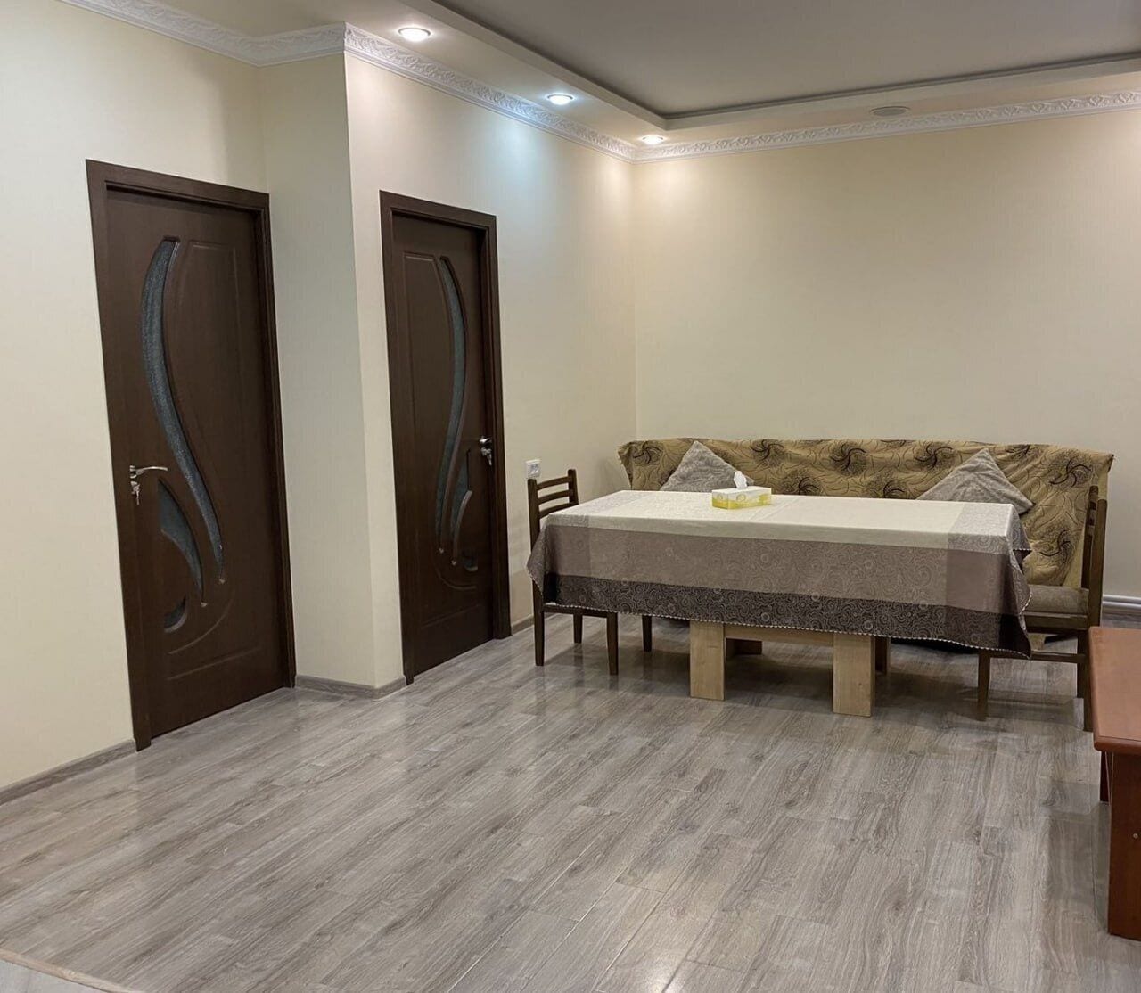 Un área de comedor con una mesa, sillas, dos puertas de madera y un sofá estampado.