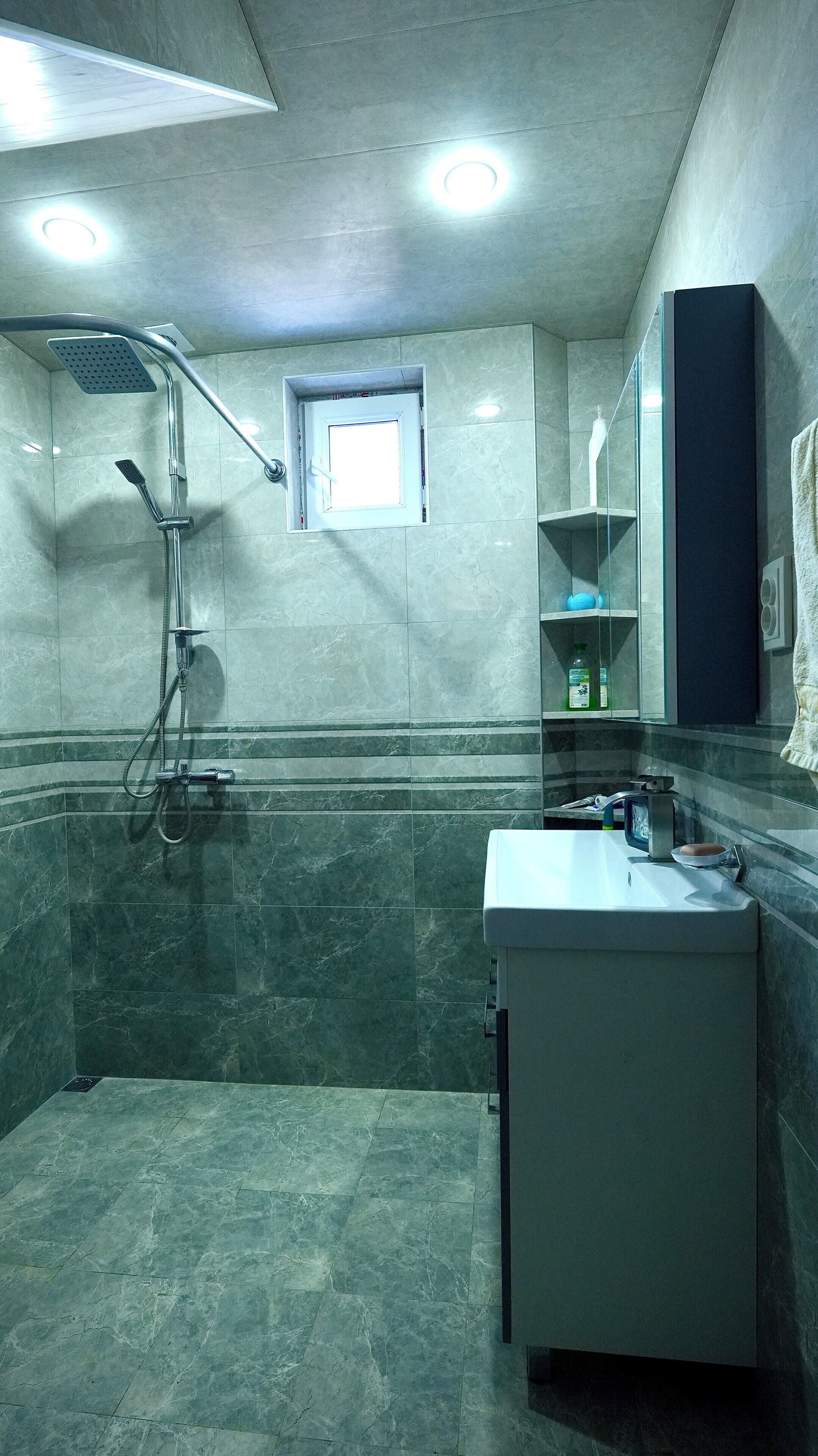 A bathroom with a shower, a sink, and a small window.