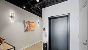 A modern hallway with a carpeted floor, a framed picture on the wall, a trash bin, and an elevator door. - The 333 Suites 204 Stay for 2 (Cincinnati)