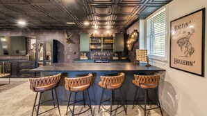 A modern kitchen with a bar area, featuring a dark ceiling, bar stools, and a framed artwork on the wall. - Stay at Wild & Blue, Log Home Retreat, Game Room w/ Arcade (White Bluff)