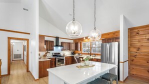 A modern kitchen with wooden cabinets, stainless steel appliances, and a central island with stools. - Stay at Wild & Blue, Log Home Retreat, Game Room w/ Arcade (White Bluff)