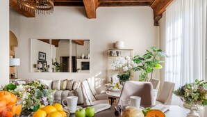 Un accogliente soggiorno con soffitto in legno, un divano, un tavolo da pranzo con frutta e una ciotola, e un grande specchio appeso al muro.