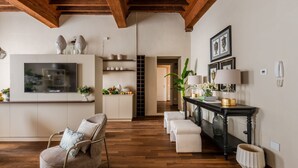 Un soggiorno moderno con parquet, una TV, un divano, un tavolo consolle con oggetti decorativi e una scala che conduce a un'altra stanza.
