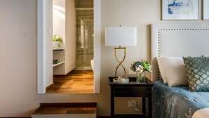A modern bedroom with a bed, a bedside table with a lamp, a vase with flowers, and a hallway leading to a bathroom. - Smart & Convenient Luxury Apartment inside Lucca (Lucca)