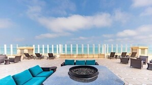 Eine Dachterrasse mit Außenbestuhlung, einer Feuerstelle und Blick auf den Ozean.