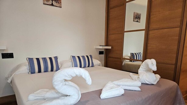 A hotel room with a large bed, striped pillows, and a wooden wardrobe. - APT Astigarraga 2H 1C (Gipuzkoa) (Astigarraga)