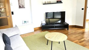 A living room with a sofa, a round table, a TV on a stand, and a bookshelf with books. - APT Astigarraga 2H 1C (Gipuzkoa) (Astigarraga)