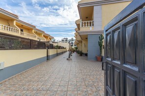 A residential area with a tiled walkway, a gated entrance, and a row of houses with balconies. - Apartment 'Los Azahares' with Sea View, Wi-Fi, and Air Conditioning (Arona)