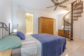 Une chambre à coucher comprenant un lit, une armoire en bois, une commode en bois, un escalier en colimaçon et un ventilateur de plafond.
