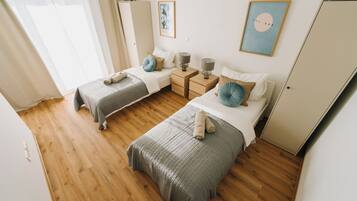 Un dormitorio con dos camas, suelo de madera, mesitas de noche con lámparas y un armario.