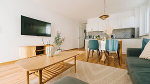 A modern living room with a wooden coffee table, a sofa, and a dining area with chairs and a small kitchen in the background. - NEW-Mia - pure relaxation in Bavaria's charm (Kemnath)