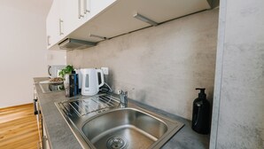 A modern kitchen with a stainless steel sink, white cabinets, and a wooden floor. - NEW-Mia - pure relaxation in Bavaria's charm (Kemnath)