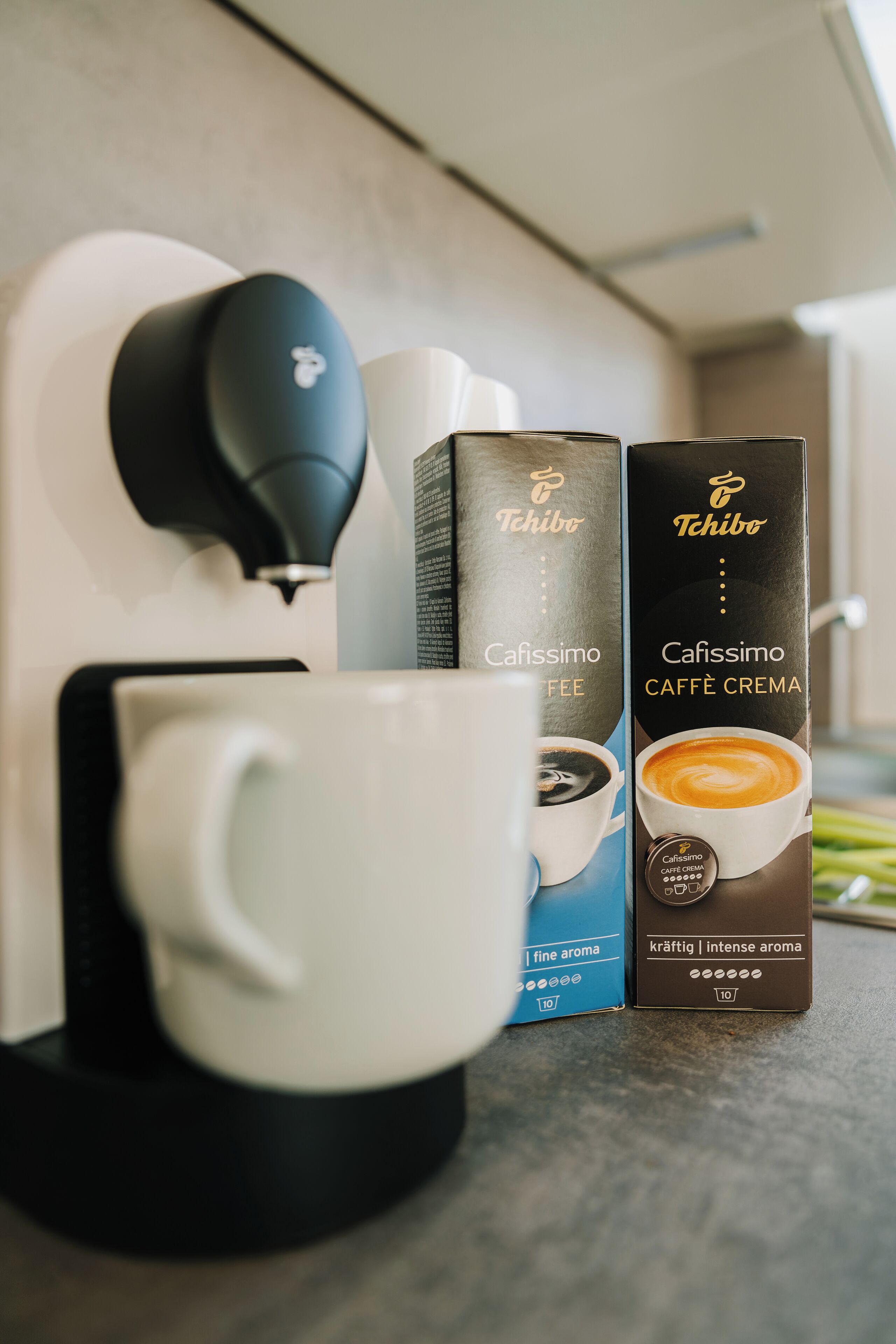 Una cafetera, dos cápsulas de café y una taza blanca sobre una encimera de cocina.