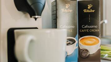 Una cafetera, dos cápsulas de café y una taza blanca sobre una encimera de cocina.