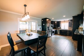 A modern kitchen with dark cabinetry, a stainless steel refrigerator, and a dining area with a wooden table and chairs.