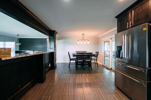 A modern kitchen with dark cabinetry, a wooden dining table, and a stainless steel refrigerator.