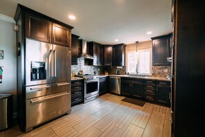A modern kitchen with dark cabinetry, stainless steel appliances, and a tiled backsplash. - The White House | Hocking Hills, Hot Tub, Theater (Logan)