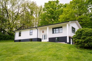 A two-story building with a white exterior and black trim, surrounded by lush greenery.