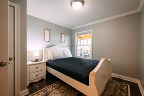 A bedroom with a bed, nightstand, dresser, and window.