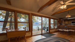 A spacious room with large windows, a wooden dining table, and a kitchen area. - Silver Bay Cabin-last minute availability 6/18 (Hague)