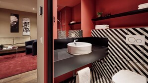 A modern bathroom with a black and white striped wall, a round white sink, and a red accent wall. - LÉGÈRE EXPRESS Hotel Leipzig - Apartment with kitchenette & breakfast optional (Leipzig)