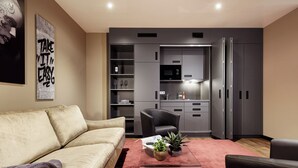 A modern living room with a sofa, a coffee table with plants, and a kitchen area with grey cabinets and appliances. - LÉGÈRE EXPRESS Hotel Leipzig - Apartment with kitchenette & breakfast optional (Leipzig)